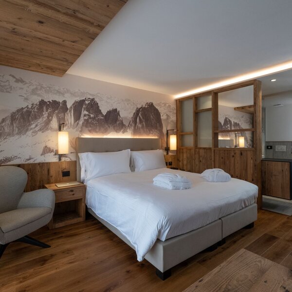 Camera di hotel arredata in legno con fotografia delle Dolomiti sullo sfondo | © Archivio Immagini ApT Val di Fassa